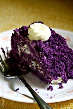 a piece of purple cake with white frosting on a plate next to a fork