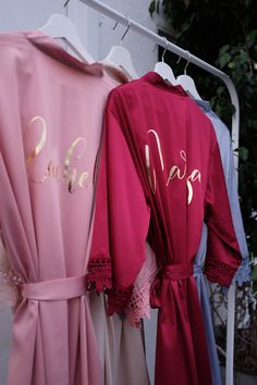 three robes hanging on a clothes rack with the word bride written in gold and pink