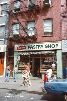 people walking on the sidewalk in front of a pastry shop