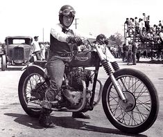 black and white photograph of a man on a motorcycle with people in the back ground