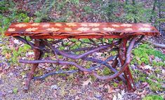 a wooden bench made out of branches in the grass and trees with leaves on it