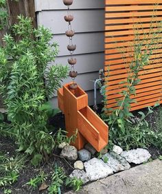 an outdoor water fountain in front of a house with rocks and plants growing around it