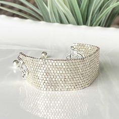 a white bracelet sitting on top of a table next to a potted green plant