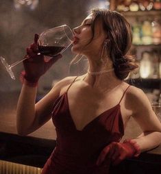 a woman in a red dress is drinking from a wine glass while standing at a bar