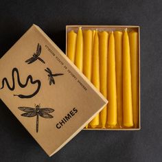 some yellow candles in a box on a black table with dragonflies and the words chimes