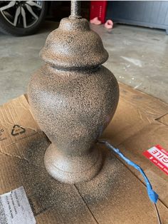 a large gray vase sitting on top of a cardboard box next to a blue cord