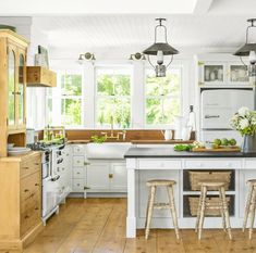 a kitchen with white cabinets and wooden flooring next to two stools in front of an island