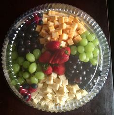 a glass bowl filled with grapes, cheese and strawberries