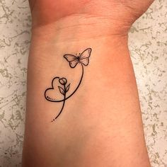 a small tattoo on the wrist of a woman with a butterfly and heart shaped flower