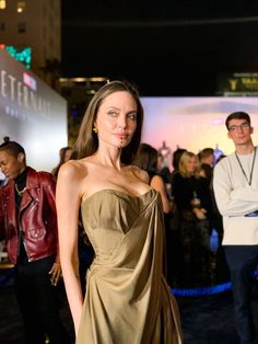 a woman in a brown dress standing on a blue carpet with other people behind her