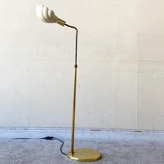 a floor lamp with a white shade on it's head and a gold base