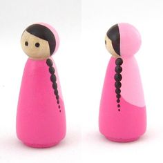 two pink wooden dolls are standing next to each other on a white surface, one has black hair and the other has brown eyes