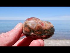 a hand holding a rock near the ocean