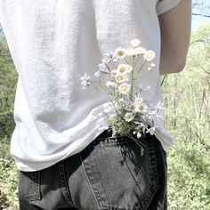 a person with their back to the camera, holding flowers in their jeans and wearing a white t - shirt