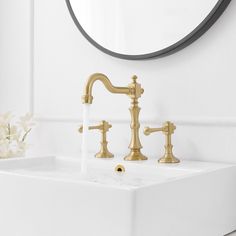 a bathroom sink with two faucets and a round mirror above it, in front of a white wall