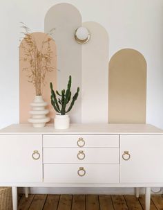 a white dresser with two vases and a plant on it in front of a wall