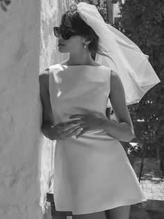 black and white photograph of a woman in sunglasses leaning against a wall wearing a wedding dress