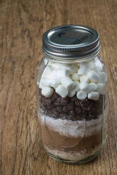 a jar filled with marshmallows and chocolate on top of a wooden table