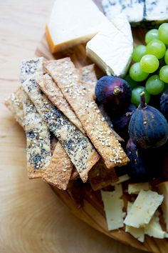 a wooden plate topped with cheese, grapes and crackers