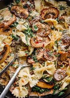 a skillet filled with pasta, mushrooms and spinach on top of a wooden table