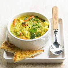 a white bowl filled with soup on top of a plate next to two spoons