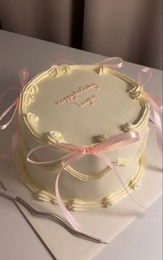 a white cake with pink ribbon on top and a knife next to it, sitting on a table