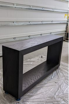 a black wooden shelf sitting on top of a white sheet covered floor next to a wall