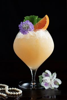 a drink in a glass with an orange and purple flower garnish