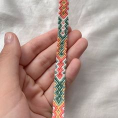 a hand holding a beaded bracelet in the shape of a cross - stitch pattern