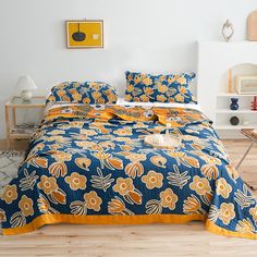 a bed with yellow and blue flowers on it in a white room next to a wooden floor