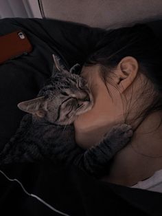 a woman laying in bed with her head on the pillow while she sleeps next to a cat