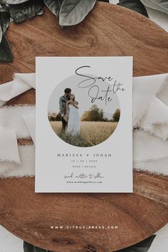 a save the date card on top of a wooden table with greenery and white ribbon