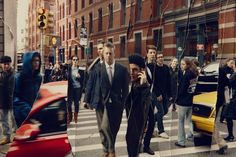 a group of people walking across a crosswalk next to cars and traffic lights on a city street