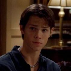 the young man is looking at something in his hand while wearing a black shirt and silver necklace