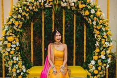 a woman in a yellow dress sitting on a bench with flowers and greenery around her