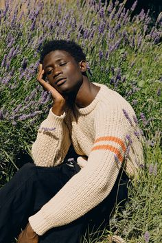 a man sitting in the grass with his hands on his face and looking at the camera