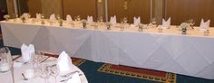 a long table is set up with white linens and place settings for the guests