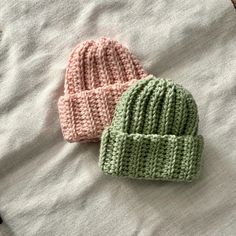 two knitted hats sitting on top of a bed