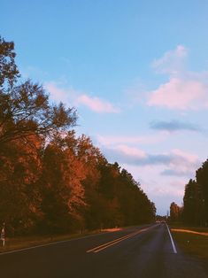 an empty road surrounded by trees with orange leaves on the sides and blue sky in the background