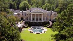 an aerial view of a large house with a pool in the front yard and trees surrounding it