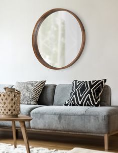 a living room with a gray couch and round mirror on the wall