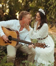 a man and woman sitting on the ground with an acoustic guitar in their hands, kissing