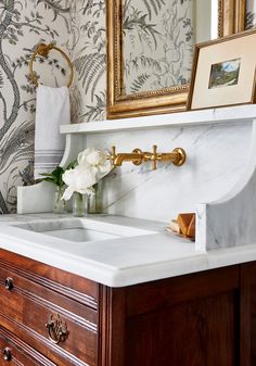 a bathroom sink sitting under a mirror next to a wooden cabinet with flowers in it