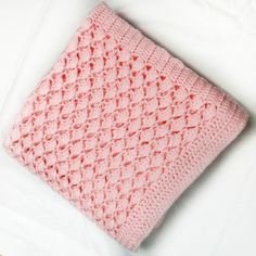 a pink crocheted blanket laying on top of a white bed next to pillows