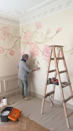 a man is painting a wall with flowers on it and a ladder in the foreground