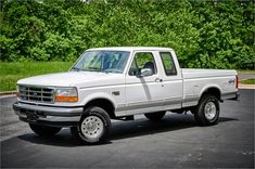 a white pick up truck parked in a parking lot next to some trees and bushes