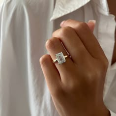 a woman's hand with a diamond ring on her left hand, wearing a white shirt