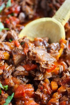 a wooden spoon in a pot filled with meat and vegetables