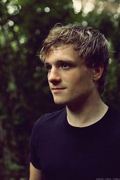 a young man is posing for a photo in front of some trees and bushes, wearing a black t - shirt