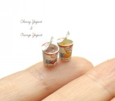 two miniature food items are sitting on someone's finger with the words cherry yogurt and orange squeezers